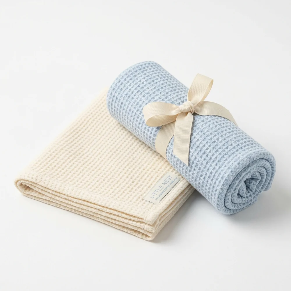 The First-Winter Swaddle in ice blue rolled with ribbon beside the cream colorway
